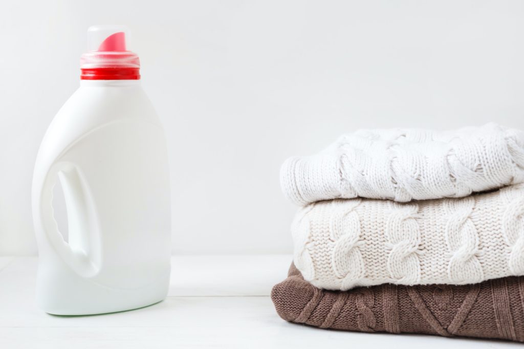 White bottle with liquid detergent and laundered flesh colored soft pullovers.